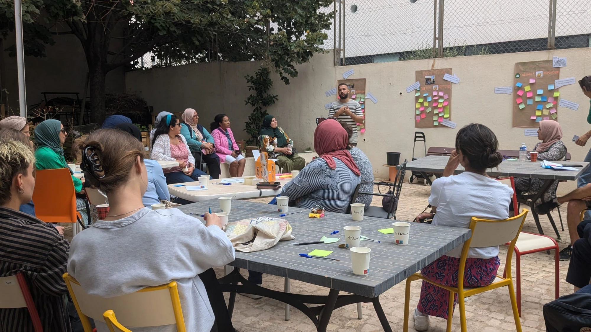 Atelier participatif en extérieur à Marseille — tables, post-its au mur et groupe d'habitantes en discussion