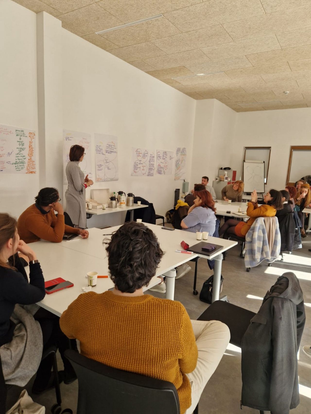 Atelier de travail collectif — salle de réunion avec schémas affichés au mur, personnes autour de tables en U
